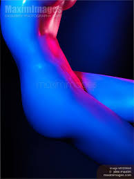 the image is a stylized, abstract photograph of a nude female body. the model is positioned at an angle, with the body curving from the upper torso to the lower legs. the lighting is highly dramatic, employing a combination of bright blue and pink neon hues. the colors are intensely saturated, washing over the body and emphasizing the curves and contours. the background is dark and indistinct, drawing all attention to the form and colors of the body. the overall style is suggestive and sensual, with an emphasis on the artistic and abstract qualities of the image rather than explicit anatomical detail. the image's smooth, almost liquid, depiction of the body may suggest a painting more than a photo.