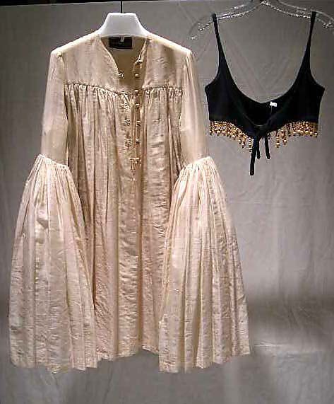 an image of a long, creamcolored dress hanging on a hanger next to a black beaded top. the dress is gathered at the top and has long, bellshaped sleeves. the top has thin straps and a beaded trim at the bottom. both items are hanging against a plain background.