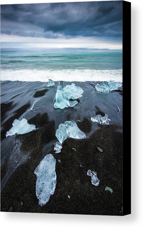 the image shows a landscape of a black sand beach with icebergs on it. the beach is on a coastline, and the ocean is in the background. the sky is cloudy.