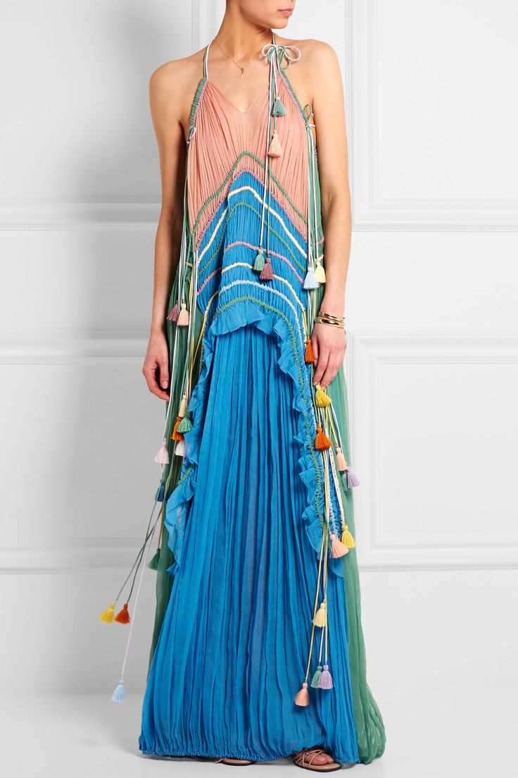 a woman in a long blue and green maxi dress with pink stripes and tassels. the dress is sleeveless and has a halter neckline. she is wearing the dress with a chic and elegant look. the dress is perfect for summer and is a great choice for a special occasion.