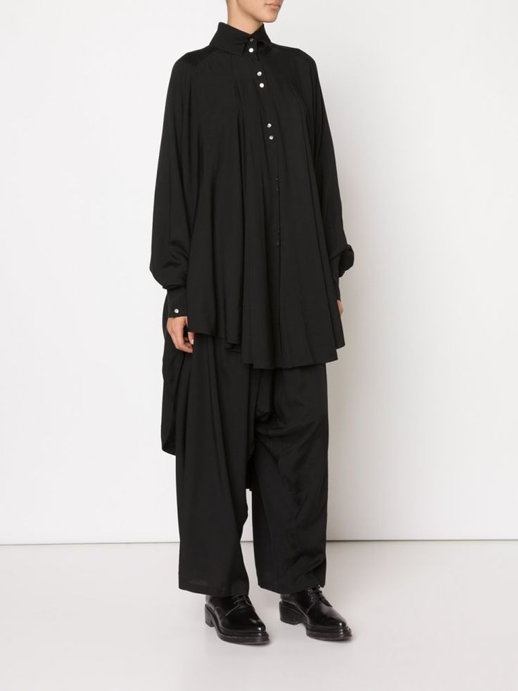 a person is standing in a black blouse, black pants, and black dress shoes.
