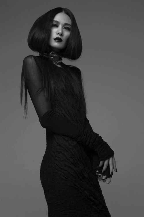 a black and white portrait of a young woman with long black hair wearing a black dress and choker. she is looking at the camera with a serious expression.