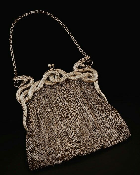 a silver chainmail purse with a detailed snake design on the frame and a chain handle. the frame features intertwined snakes with their heads facing outwards. the purse has a simple clasp. the background is black.