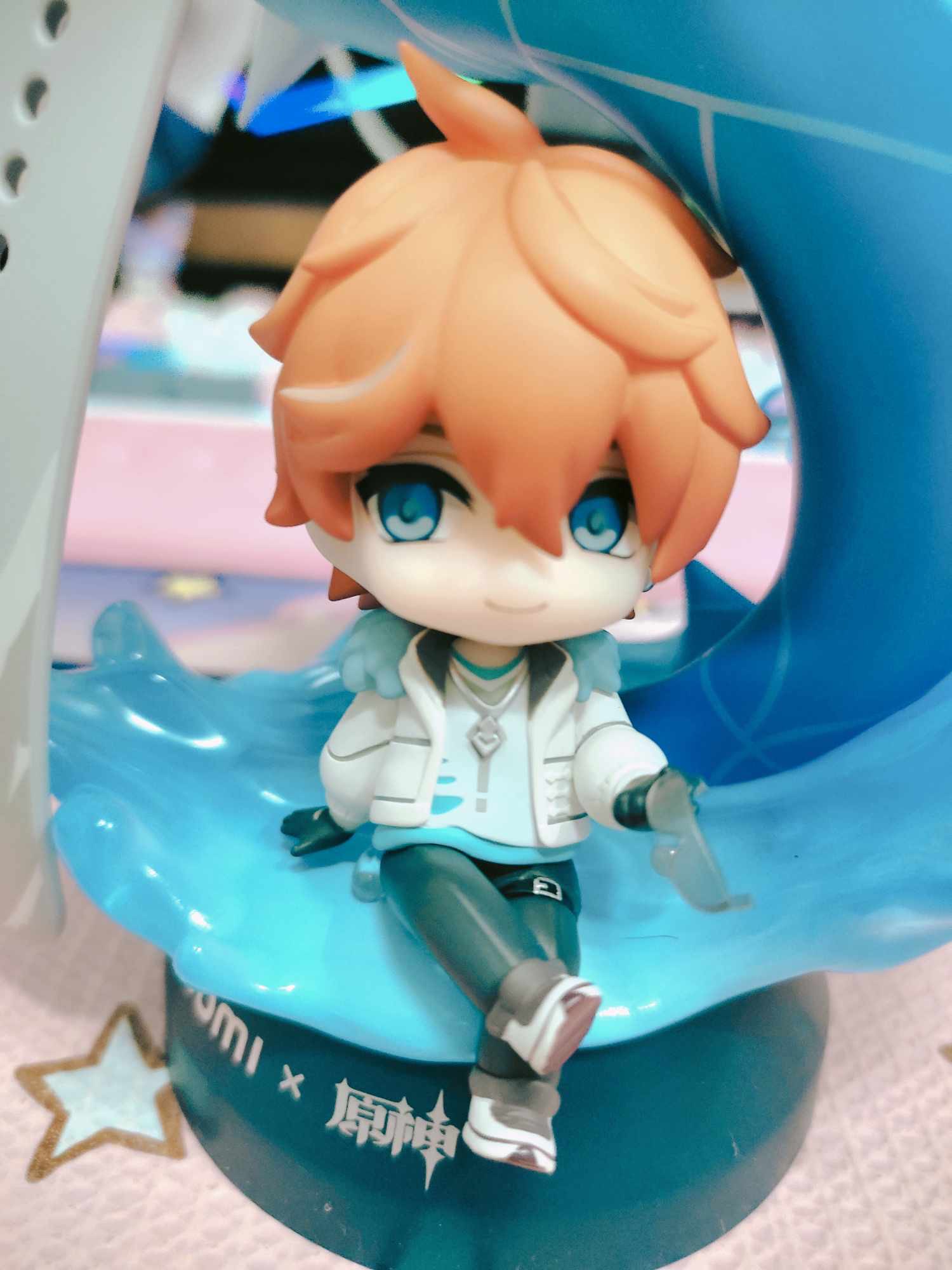this is a figurine of an anime character. the character is a young male with orange hair and blue eyes. he is smiling and sitting on a blue waveshaped base. he is wearing a white jacket and black pants. the figurine is made of plastic and is about 3 inches tall.