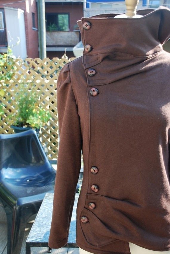 a closeup of a brown jacket with a high turtleneck collar and buttons down the side. the jacket is made of a soft, stretchy fabric and has a casual, relaxed fit. it's perfect for fall and winter.