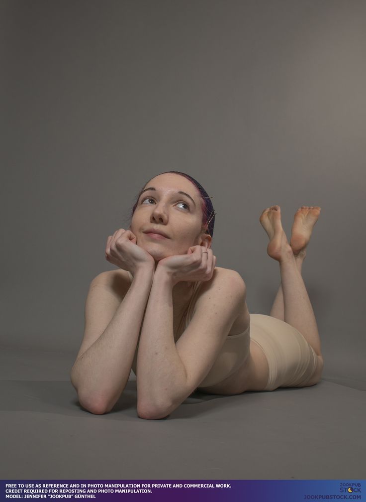 a young woman with dyed purple hair pulled back lies on her stomach on a seamless gray background. she is resting her chin on her hands, gazing upwards with a thoughtful expression. the soft lighting and her relaxed posture create a serene and contemplative atmosphere. she is wearing a simple, lightcolored top and shorts.  the image is a studio shot likely intended as a reference for artists.