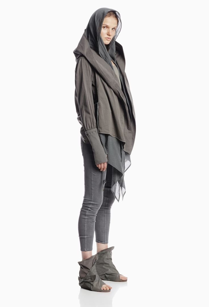 a woman with blonde hair is wearing a gray hoodie and matching pants. the hoodie is worn like a scarf and drapes around her neck and down to her waist. she is also wearing gray boots. the woman is standing on a white background and is looking towards the camera.