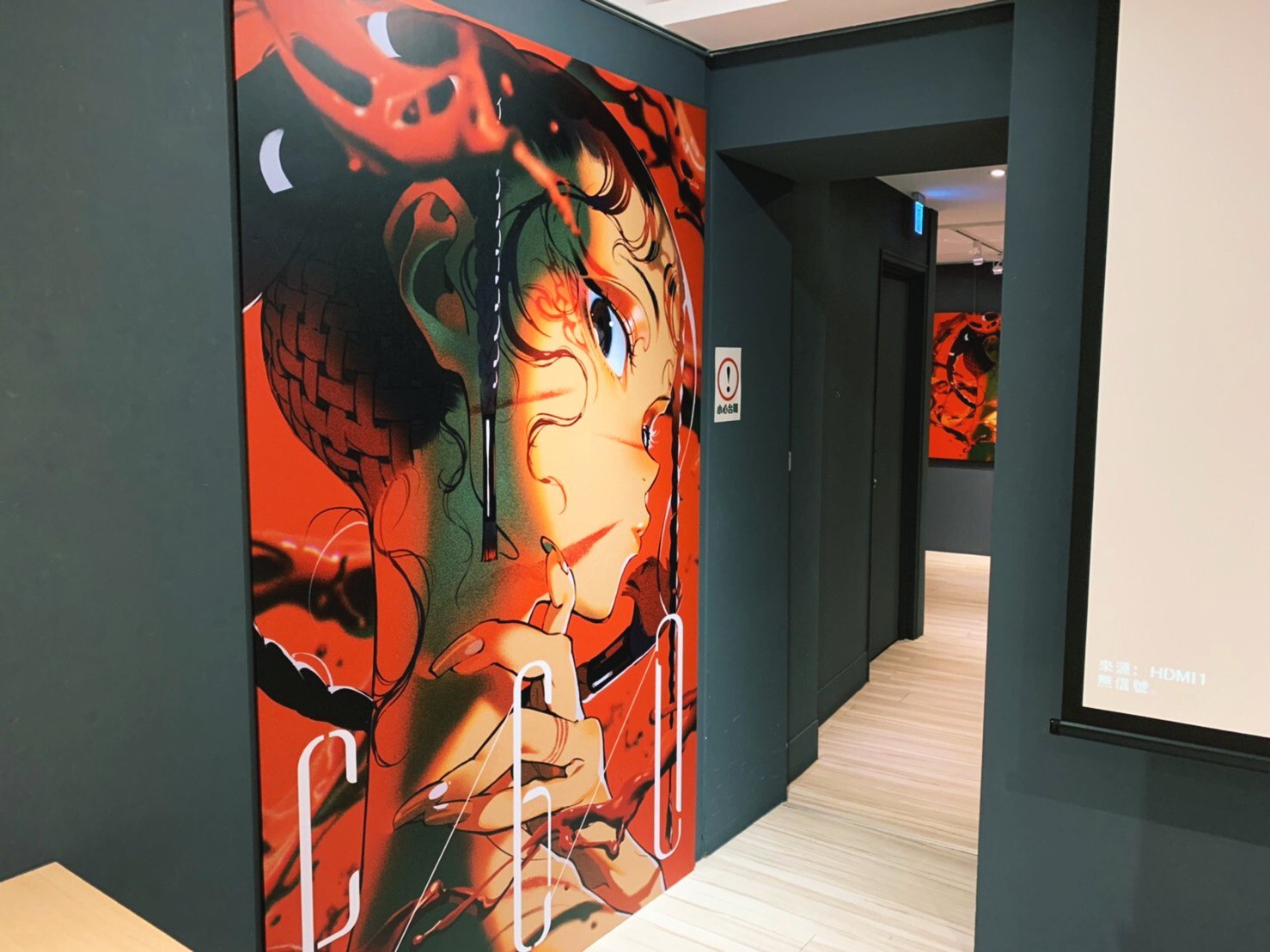a vibrant, eyecatching illustration of a woman with elaborate hair and makeup is displayed prominently on the wall of an indoor space, likely a gallery or exhibition dedicated to art, graphic novels, or anime. the artwork features a bold color scheme with black, white, and red being predominant. the perspective is from eye level, giving the viewer a sense of walking into the space and being greeted by the artwork.