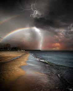 a picturesque scene of a vibrant rainbow arching across a stormy sky as lightning strikes in the distance. the beach stretches out towards the choppy sea, the sandy shore contrasting with the dark, swirling clouds above. the image captures the dramatic beauty of nature's power, showcasing the vibrant colors of the rainbow against the backdrop of a stormy sky.