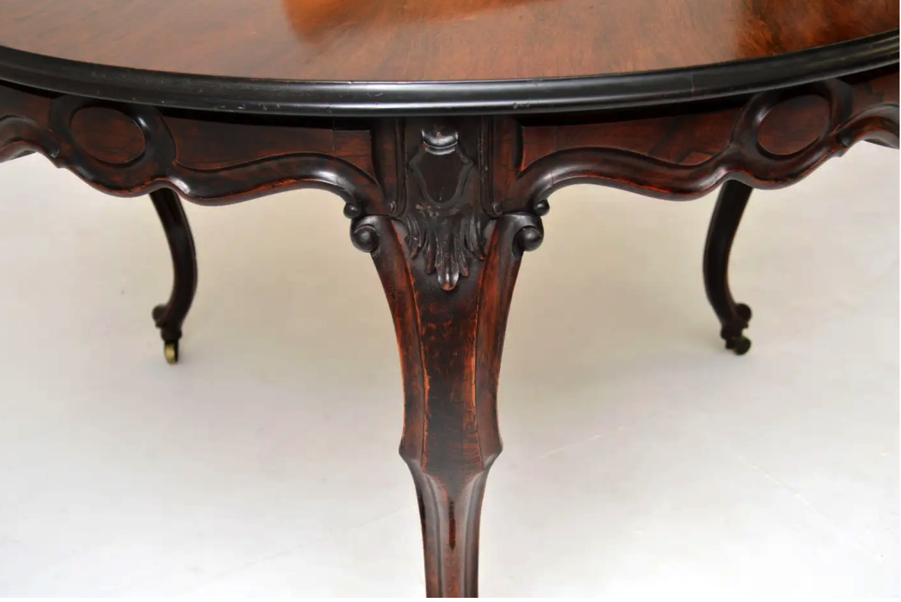 a closeup shot of an antique, ornate, round table made of wood, with intricate carvings on the legs. the table appears to be made of mahogany and features a dark brown finish with a black edge. the table legs are elegantly curved and decorated with rococostyle designs. the table is situated on a white surface, highlighting its intricate details and craftsmanship. it's an antique piece showcasing the beauty of victorianera furniture.