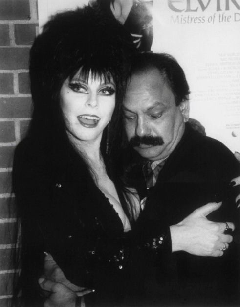 a black and white photo of elvira, mistress of the dark, and a man posing for a photo.