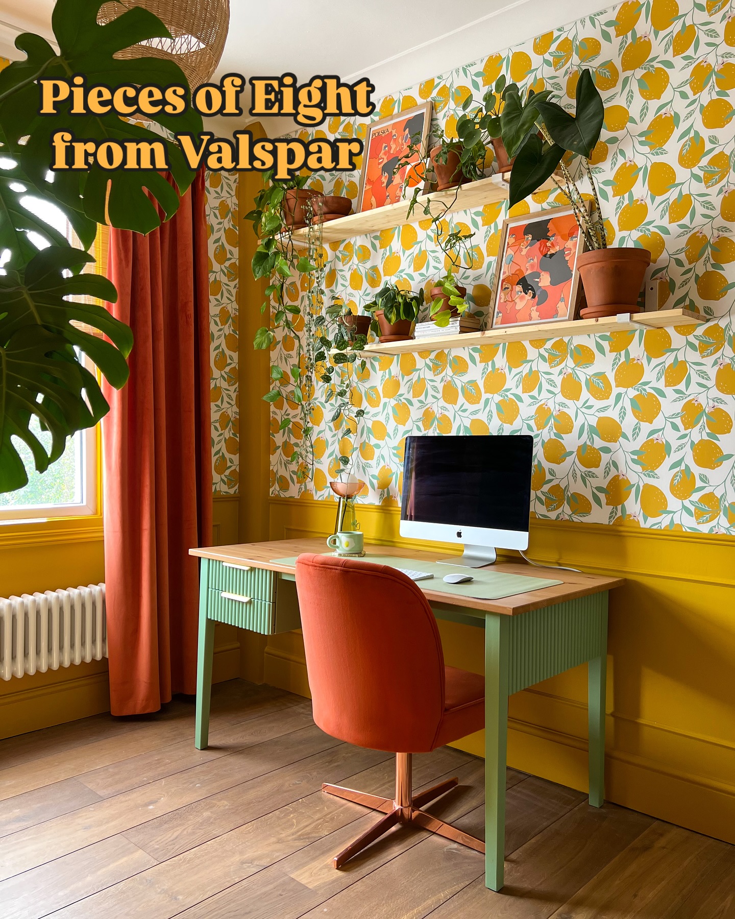 an interior shot of a room with a desk, chair, plants, paintings, wallpaper, and shelves. the desk is a light wood color with green legs and a green drawer. the chair is orange and has a coppercolored base. there are plants on the desk and on the shelves above the desk. the wallpaper is a lemon print. the curtains are orange. the floor is wood. the text "pieces of eight from valspar" is also present.