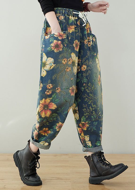 a closeup shot showcases a woman's lower body, clad in loosefitting, floralprinted denim pants. the pants feature a drawstring waist and multiple pockets. the pants are a relaxed, wideleg style that falls loosely around her ankles. she is wearing black ankle boots and the overall style is relaxed and casual. the background is plain and simple, allowing the pants and boots to stand out.  the image highlights the pants' unique floral pattern and loose silhouette.
