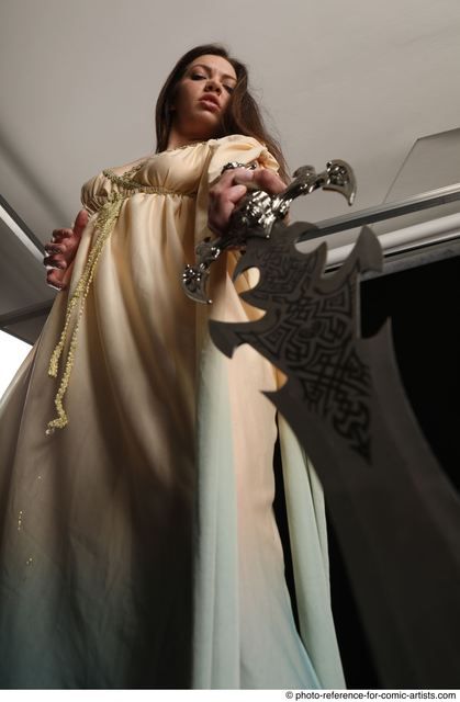 a woman, dressed in a long white gown, is standing with a large, intricate sword in her hand. her eyes are focused, and she is looking up at the camera. the lighting is low key, creating a dramatic and shadowy effect. the image suggests that she is a powerful and skilled warrior.