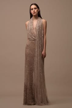 a woman in a sparkling sequined dress poses elegantly for the camera. she is wearing a long, flowing gown with a plunging neckline and a high slit. her hair is styled in a simple updo and her makeup is natural and polished. the gown shimmers in the studio lighting, making her look absolutely stunning.