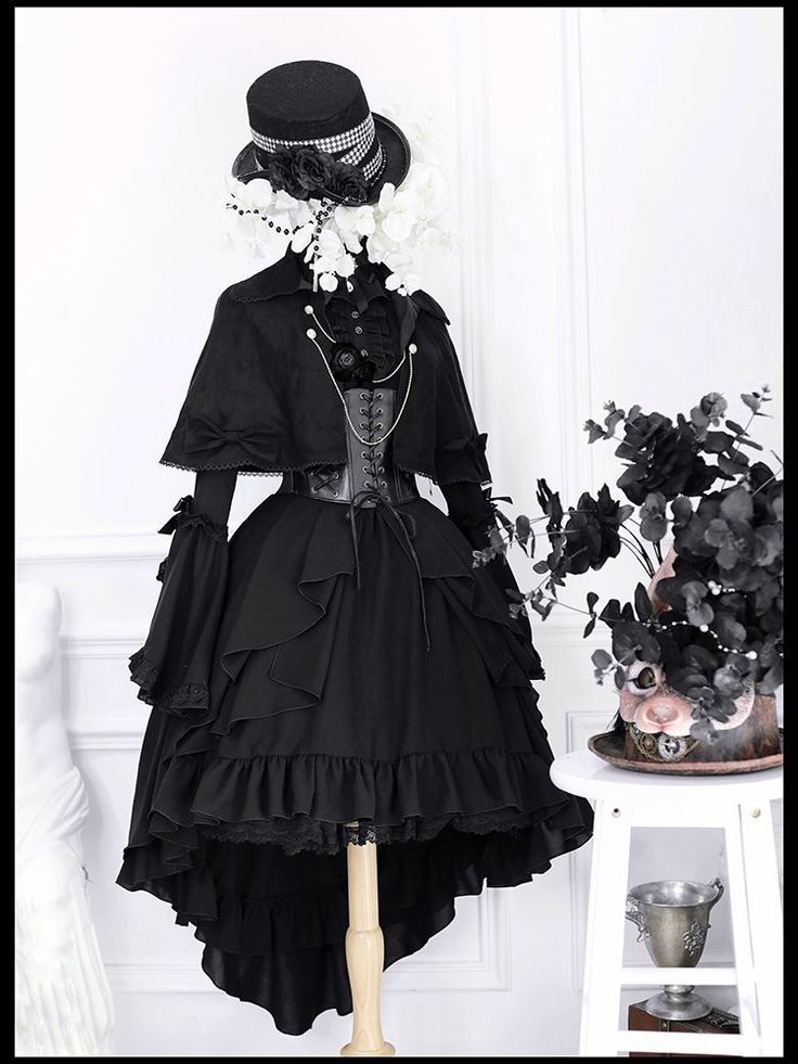 the image showcases a black gothic lolita dress displayed on a mannequin. the dress features a highlow skirt with multiple layers of ruffles and lace detailing.  a black cape with bow accents is worn over the dress, and a black corset is visible underneath. a top hat adorned with white flowers sits atop the mannequin's head. the overall style is a blend of gothic, victorian, and steampunk aesthetics, with a dark and elegant feel. the backdrop is simple, with white walls and a white side table featuring a small decorative piece.  the image is welllit and professionally styled, highlighting the details of the outfit.
