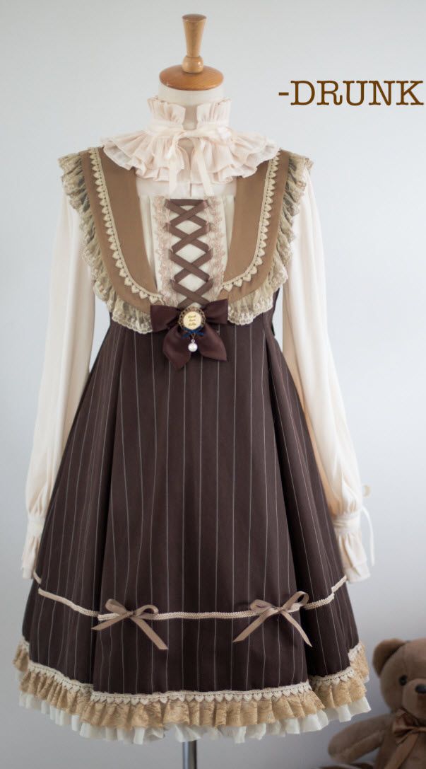 a brown and cream lolita fashion dress is shown on a mannequin. the dress has a brown pinstriped skirt, a cream bodice with brown accents, and lace trim. there is a teddy bear partially visible to the right.