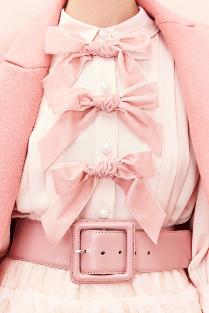 loseup view of a woman's outfit featuring a pale pink coat, a white blouse adorned with three large, layered pink satin bows, and a wide pink belt with a square buckle. the overall aesthetic is very feminine, delicate, and pasteltoned. the focus is on the intricate details of the bows and the coordinating colors of the outfit. the image exudes a sense of elegance and luxury. the light and airy feel of the fabric is prominent.