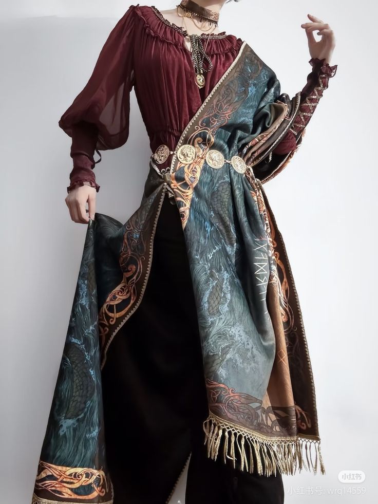 a woman wearing a maroon blouse with ruffled neckline and sheer, billowy sleeves is posing in front of a white wall. the blouse is complemented by a choker and a layered necklace with coinlike pendants. she is wearing a coin belt and a long shawl with a detailed design, draped over her shoulders and waist. the shawl has fringe at the bottom. the rest of her outfit consists of a long black skirt or pants, which are only partially visible due to the shawl.
