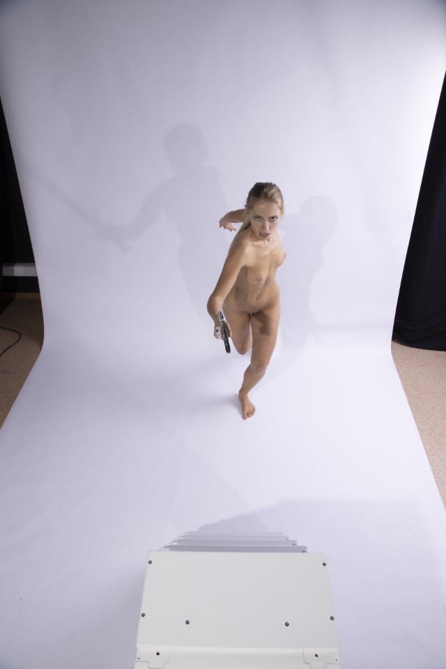 a nude woman is running in a studio, holding a gun. she is on a white background.