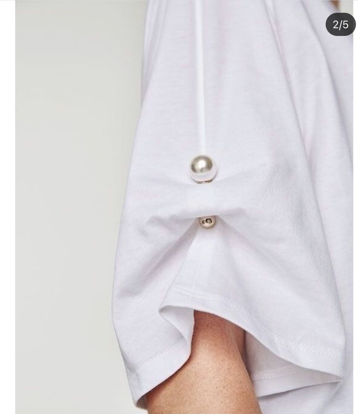 a closeup shot of the rolledup sleeve of a white tshirt. the sleeve is secured by a pearllike button and the arm is visible.