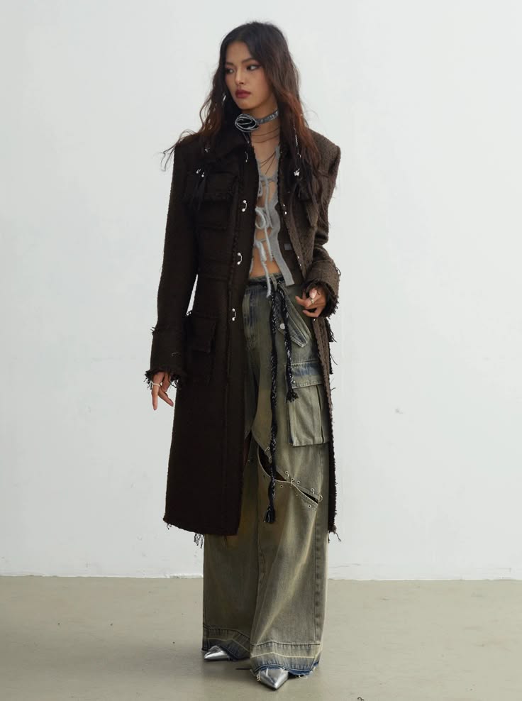 a fashion model wearing a long brown coat and ripped jeans, accessorized with a black choker and silver high heels. she is posing in a stylish street style fashion.