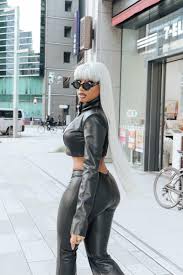 a stylish woman poses on a city street in tokyo. she is wearing a black leather crop top and matching pants, with her long white hair styled straight. she is also wearing sunglasses and has her back turned slightly towards the camera. the background is blurred, highlighting the woman and her outfit.  the overall vibe is chic and modern.