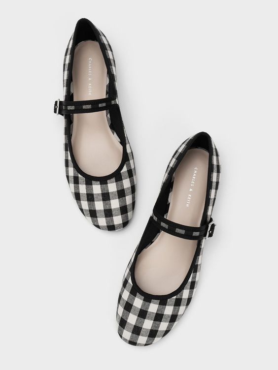 a pair of charles & keith women's black and white gingham mary jane flats are shown.  the shoes are positioned slightly angled, with one shoe above the other. they have a simple design with a small strap across the instep. the gingham pattern is clearly visible. the shoes appear to be made of a lightweight fabric.