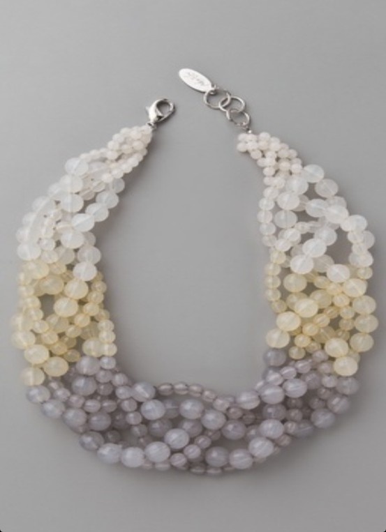 a multistrand ombre necklace with silver clasps. the necklace is made of white, cream, and gray beads. the beads are arranged in a graduated ombre pattern, starting with white at the top and ending with gray at the bottom. the necklace is a beautiful and elegant piece of jewelry that would be perfect for any occasion.