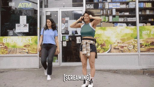two women stand outside a grocery store. one is walking past the store and looks annoyed, and the other is standing in front of the store with her hands on her head and appears to be screaming. the store has a sign for an atm and a breakfast menu on the window.