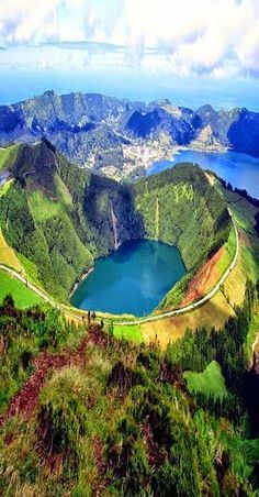 an aerial view of a volcanic crater lake nestled in the heart of a lush, green island. the lake is a vibrant blue, surrounded by verdant slopes and a ring of mountains. the sky is a clear blue, with fluffy white clouds adding a touch of drama. the scene is breathtakingly beautiful, with a sense of peace and tranquility.