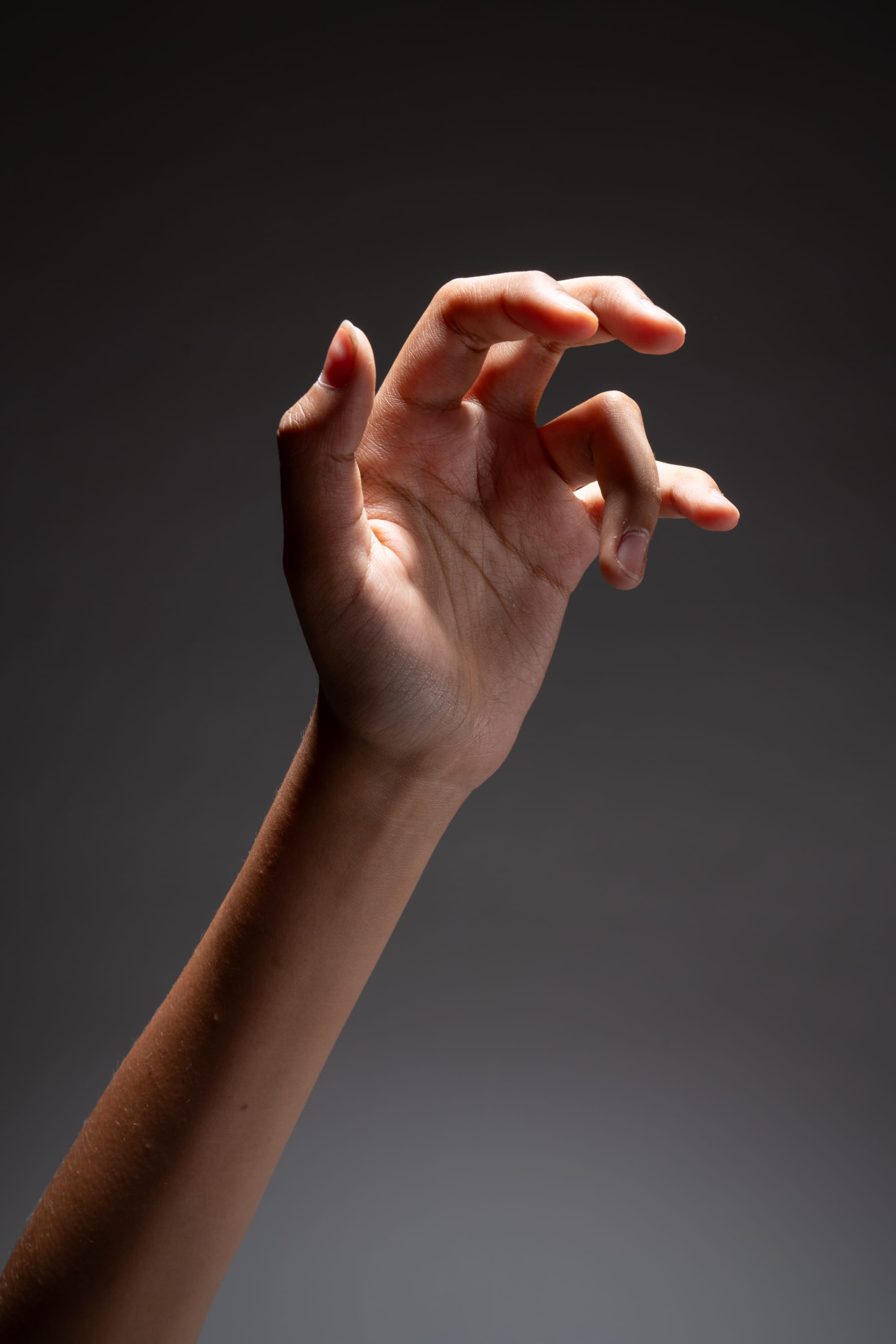 a hand reaching out from a dramatically lit arm against a dark gray background. the hand is posed in a grasping or clutching gesture.