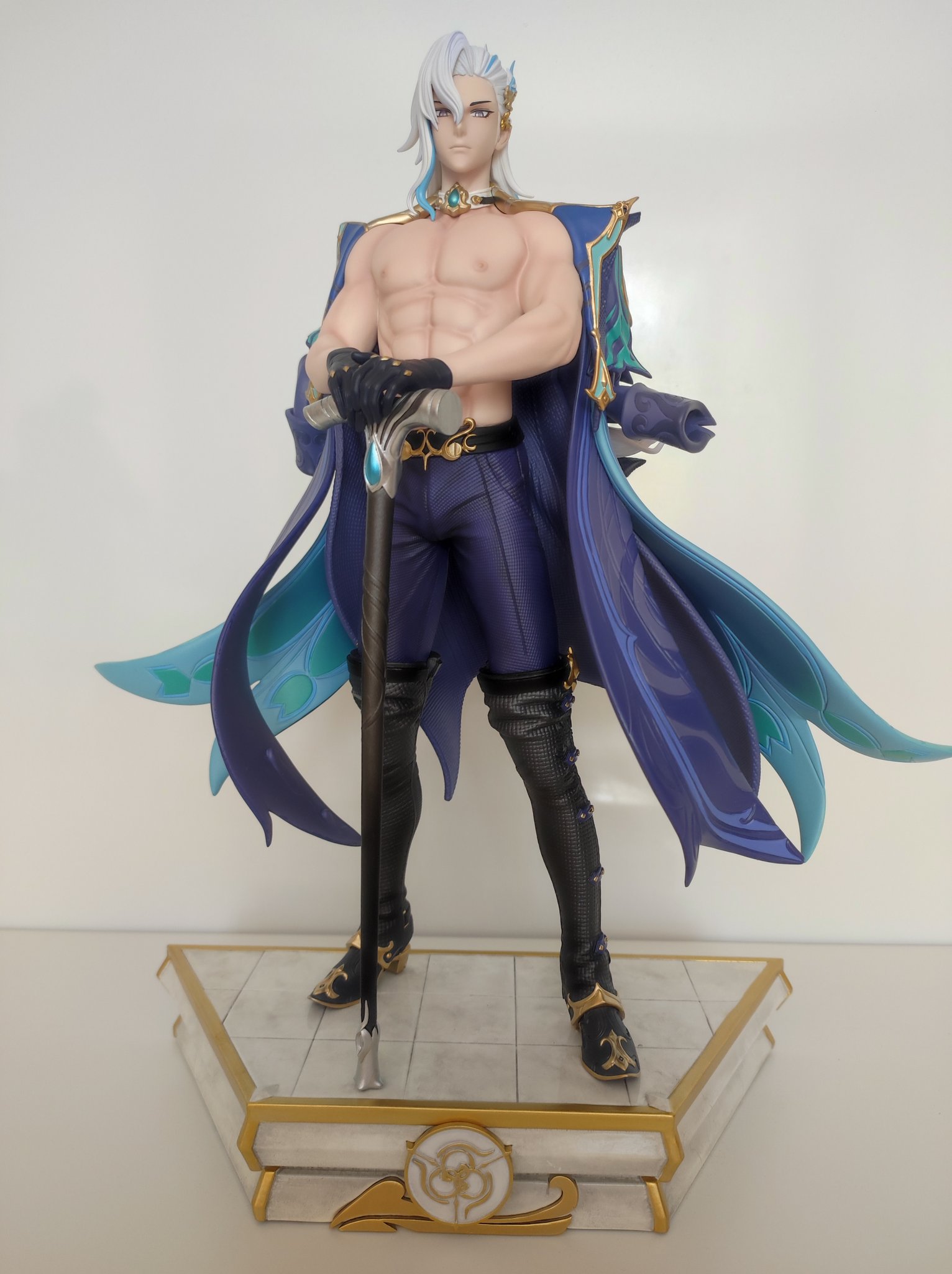 a figurine of a male anime character in a blue and purple outfit with white hair and a cane, standing on a square base. the figurine is highly detailed and appears to be of high quality.