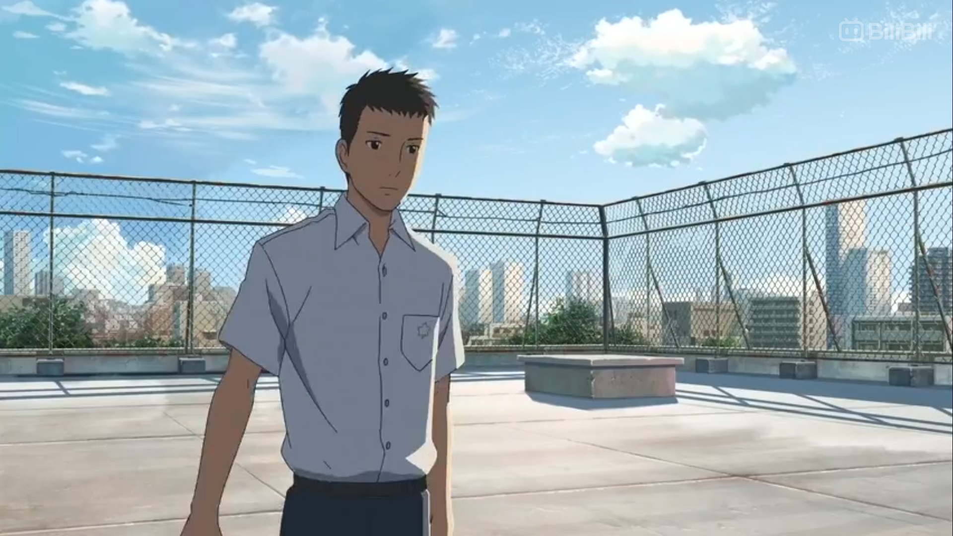 this is an outdoor scene from an anime. a young man in a school uniform stands on a rooftop in the daytime. in the background, a chain link fence surrounds the rooftop, and behind that, you can see a cityscape with many buildings under a bright blue sky with some clouds.
