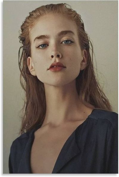 a closeup portrait of a young woman with long reddishblonde hair and striking blue eyes. she has a serious expression and is wearing a dark blue vneck top. the lighting is soft and diffused, creating a sense of intimacy. the background is a neutral beige color, which allows the focus to remain on the woman's face and upper body.