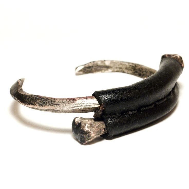 a closeup shot of a silver and leather bracelet. the bracelet is made of two silver pieces that are curved to form a circle. the leather is wrapped around the silver, and the ends of the leather are stitched together. the bracelet is minimalist and edgy, and would be a great addition to any wardrobe.