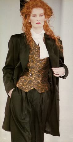a woman with red hair wearing a black suit, white collar and black pants, she's posing in a studio.