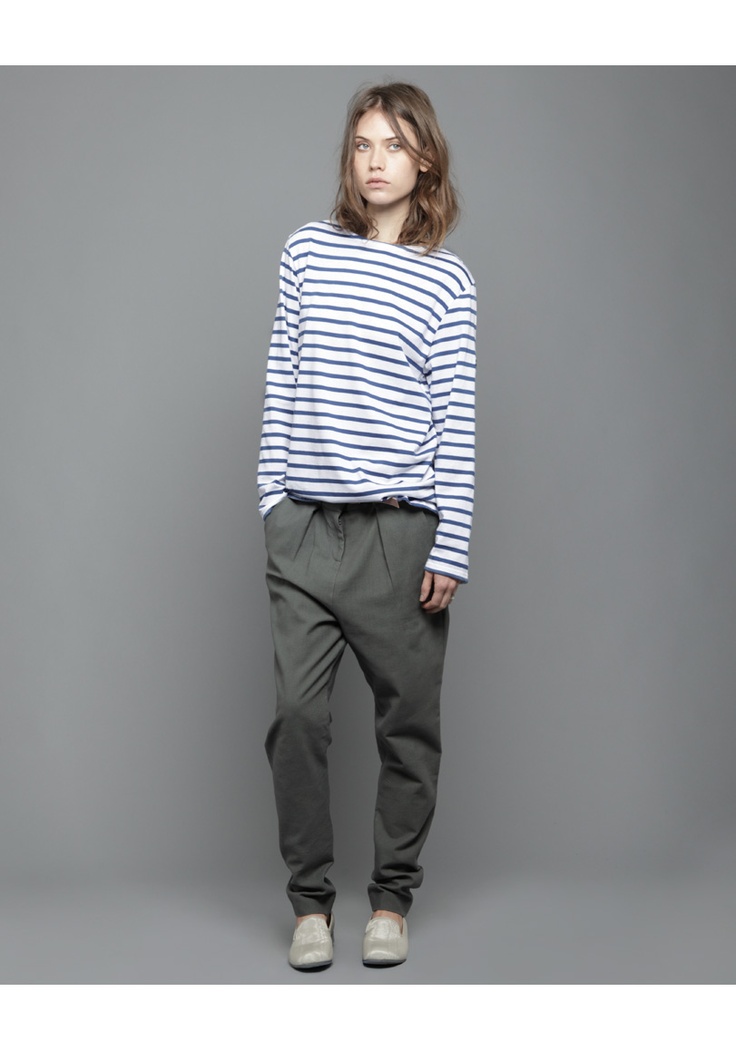 a fullbody shot of a woman model standing against a grey background. she's wearing a navy and white striped longsleeved shirt and olivegreen haremstyle pants. the model is wearing lightcolored flat shoes. the image showcases casual, relaxed style of clothing.