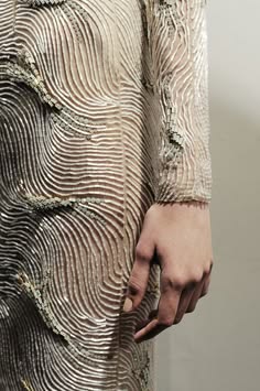 a closeup of a woman wearing a silver sequined dress with a unique pattern. the dress has intricate embroidery and a wavy design. the sleeve is made of the same material as the dress and creates a beautiful contrast. the woman's hand is visible, resting on the fabric, showcasing the texture and detail of the garment. the image captures the elegance and sophistication of highfashion design.
