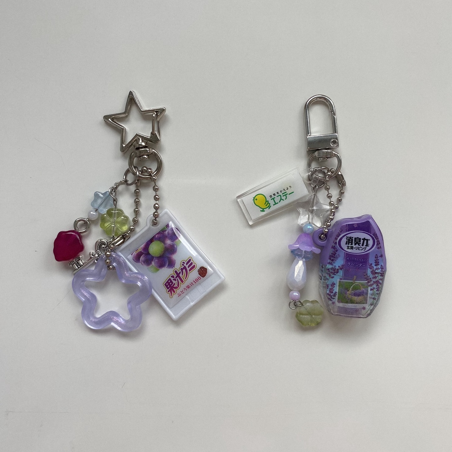 two keychains with charms and beads on a white surface. the keychain on the left has a star shaped top, a bag of grape gummies, and other various beads and charms. the keychain on the right has a hookshaped top, ester brand charm, lavender air freshener, and assorted beads.