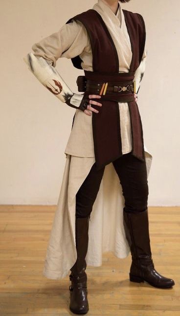 a person cosplaying as a jedi from star wars. they are wearing a brown and white robe with a belt and boots. they are also holding a lightsaber.