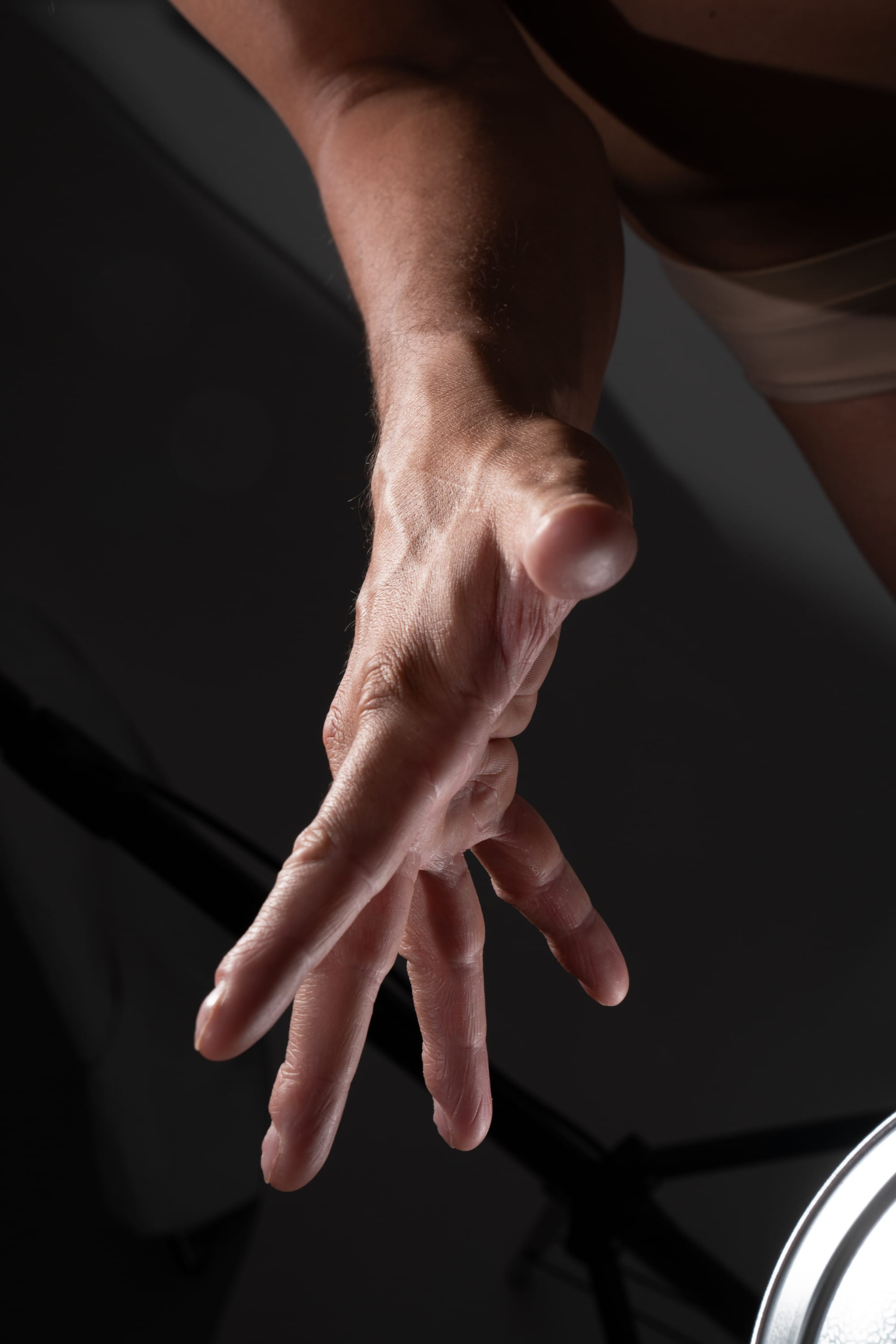 the image shows a closeup of a man's hand reaching down towards a bright light source. the lighting creates dramatic shadows and highlights on the hand, emphasizing the texture and form of the skin and fingers. the image uses a worm'seye perspective, giving a unique and dynamic view of the hand.