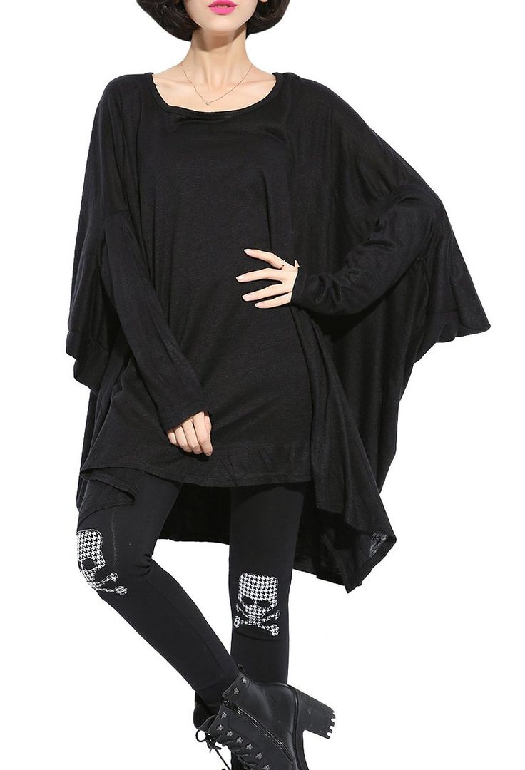a woman is wearing a black outfit consisting of an oversized tunic, leggings with skull prints on the knees, and black boots. the tunic is loose and asymmetrical, and she has her hand raised in a casual pose. the leggings are black with white and black checkered skull and crossbones patches on the knees. the boots are black leather and have a chunky heel. the background is white.
