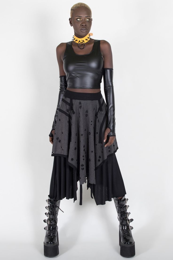 a fullbody studio shot of a darkskinned woman with short hair, wearing a black leather top, a layered grey and black skirt, long black gloves, and black platform boots. she is accessorized with a yellow spiked choker. the background is plain white, and the model's pose is slightly angled, looking to her right.  the overall style is punk or gothinspired, featuring dark colors and edgy elements.