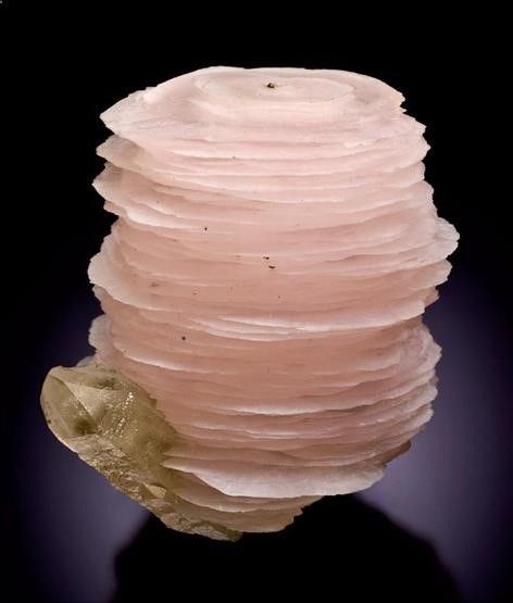 a close up of a pink calcite crystal with several layers. it is a pink mineral with several layers that resembles a cake. the crystal is very detailed and almost appears to be glowing.