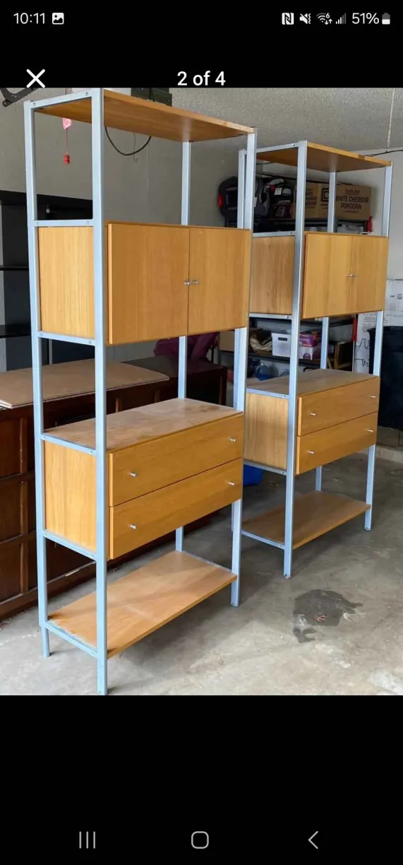 two matching shelving units stand side by side. they feature a lightcolored wood finish with metal frames. the units have a combination of shelves, cabinets, and drawers for storage. the style appears to be midcentury modern or retro.