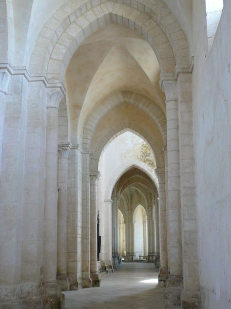 this image shows a long hallway within a church or abbey. the hallway is lined with columns and arches made of lightcolored stone. sunlight is streaming in from the far end of the hall illuminating the scene.