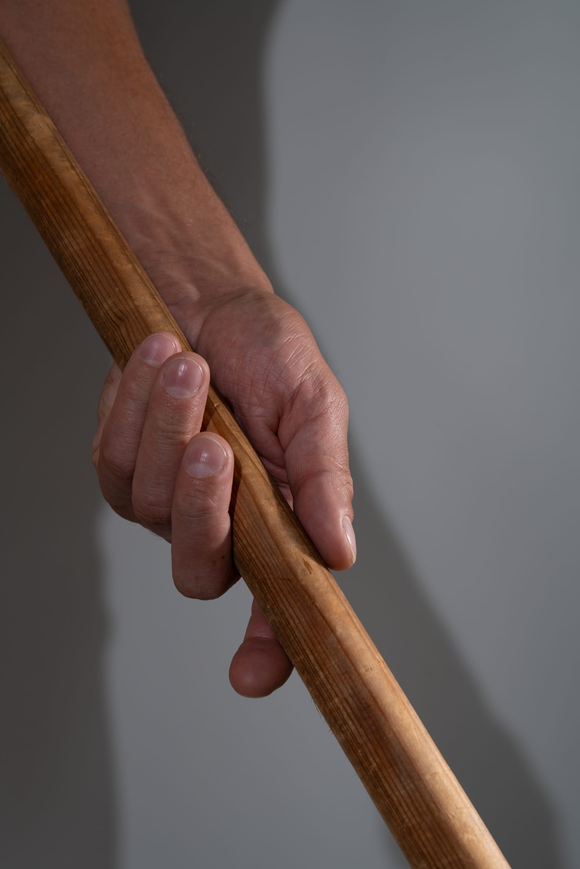 a closeup of a man's hand tightly gripping a wooden stick or pole. the image highlights the texture of the wood and the strength of the grip. the lighting creates a sense of drama and emphasizes the contours of the hand and stick.