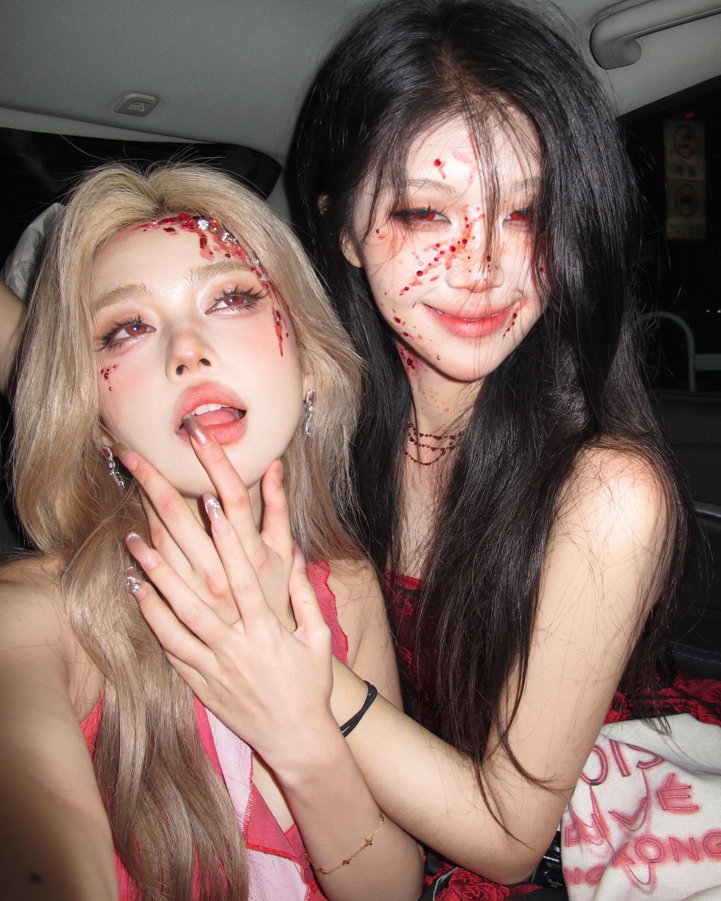 the image shows two women in a car, presumably on their way to a halloween party. they are both wearing red, halloweenthemed costumes and have their faces done up with spooky makeup. they are posing for a selfie, both looking at the camera.