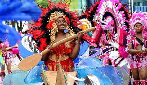 a vibrant carnival parade with women in colorful costumes and feathered headdresses.  the parade is full of energy and joy, with the women dancing and celebrating.  the costumes are intricate and beautiful, and the colors are eyecatching. the street is lined with spectators,  who are enjoying the spectacle. this is a typical carnival scene, full of life and excitement.